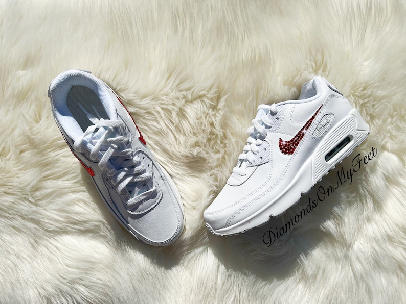 May include: White leather sneakers with a red rhinestone Nike swoosh. The shoes are on a white fluffy surface. The text "Diamonds On My Feet" is visible in the lower right corner of the image.