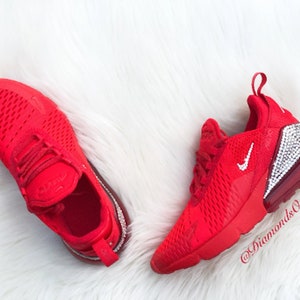 May include: Red Nike Air Max 270 sneakers with a white swoosh and a crystal-encrusted heel. The shoes are on a white fluffy surface. @DiamondsOnMyFeet