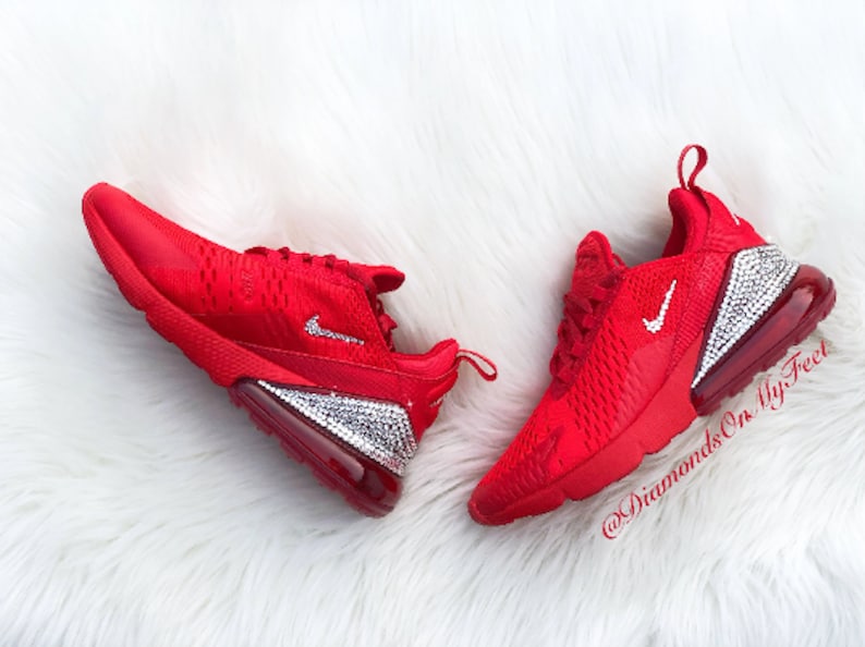 May include: Red Nike Air Max 270 sneakers with a crystal-encrusted sole and a white Nike swoosh logo. The shoes are on a white fluffy surface. The text "@DiamondsOnMyFeet" is visible on the right shoe.