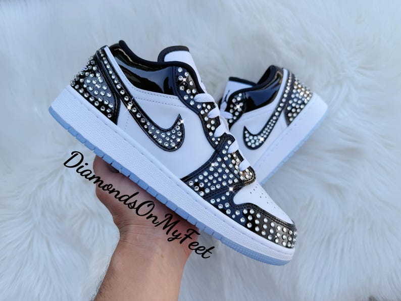 May include: White and black sneakers with crystal embellishments. The shoes feature a black patent leather overlay and a crystal-studded Nike swoosh. The text "DiamondsOnMyFeet" is visible on the side.