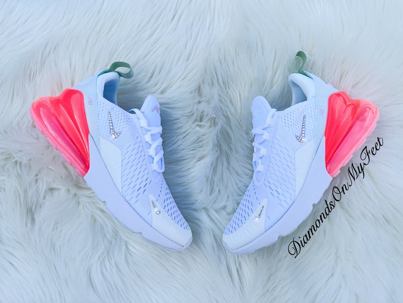 K&ouml;nnte beinhalten: Paar wei&szlig;e Sportschuhe mit einem hellblauen und rosa Farbverlauf. Die Schuhe haben ein kristallbesetztes Nike-Logo und Akzente. Der Text "Diamonds On My Feet" ist auf dem rechten Schuh sichtbar.