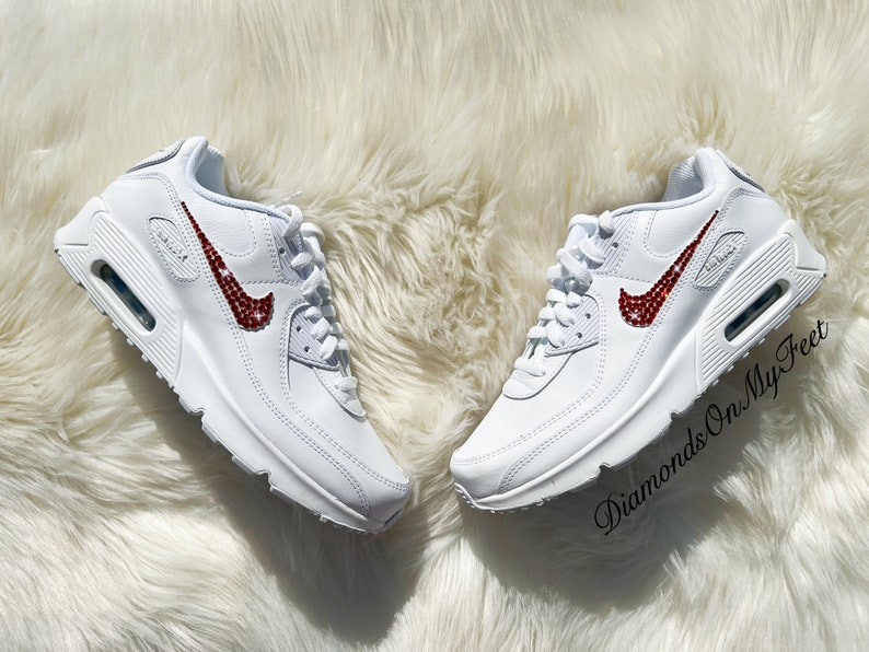 May include: White leather sneakers with a red rhinestone Nike swoosh. The shoes are on a white fluffy surface. The text "Diamonds On My Feet" is visible in the lower right corner of the image.