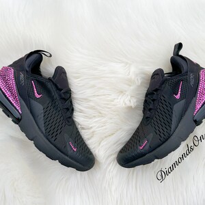 May include: Black Nike Air Max 270 sneakers with pink rhinestones on the heel and swoosh logo. The sneakers have a black mesh upper and a white fuzzy background.