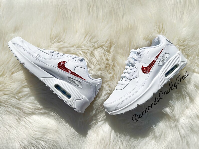 May include: White leather sneakers with a red rhinestone Nike swoosh. The shoes are on a white fluffy surface. The text "Diamonds On My Feet" is visible in the lower right corner of the image.
