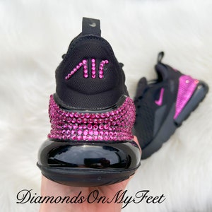 May include: Black Nike Air Max 270 sneakers with pink rhinestones covering the entire shoe. The Air Max logo on the back of the shoe is also covered in pink rhinestones.