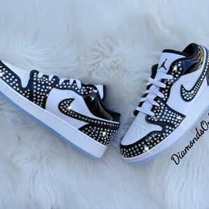 May include: A pair of white and black sneakers embellished with rhinestones. The shoes feature a white base with black accents and a sparkling rhinestone pattern. The soles are white with a light blue tint. The text "DiamondsOnMyFeet" is visible.
