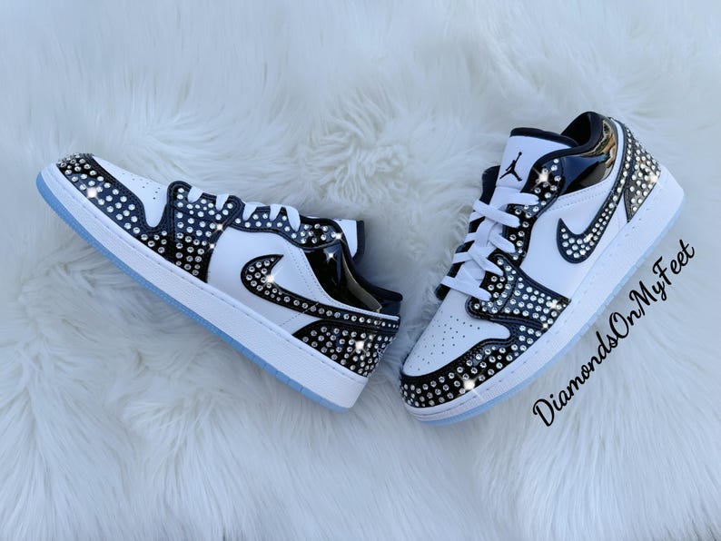 May include: A pair of white and black sneakers embellished with rhinestones. The shoes feature a white base with black accents and a sparkling rhinestone pattern. The soles are white with a light blue tint. The text "DiamondsOnMyFeet" is visible.