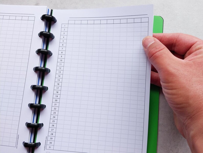 Puede incluir: Un cuaderno blanco con una encuadernaci&oacute;n en espiral negra y un patr&oacute;n de cuadr&iacute;cula en las p&aacute;ginas. El cuaderno est&aacute; abierto en una p&aacute;gina con los n&uacute;meros del 1 al 31 listados en el lateral.