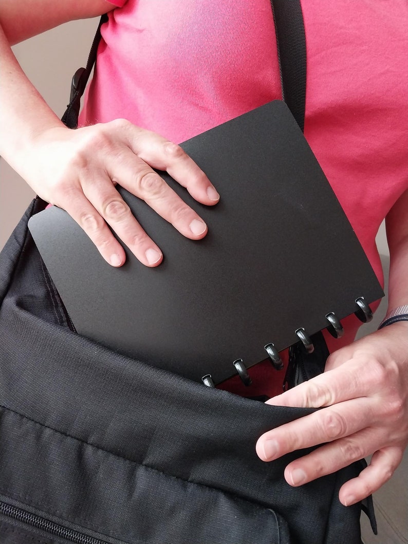Puede incluir: Un cuaderno negro con encuadernaci&oacute;n en espiral se coloca en una mochila negra.
