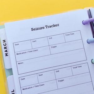 Könnte beinhalten: Eine weiße Seite mit einem hellvioletten und blauen Binder. Die Seite trägt den Titel "Seizure Tracker" und hat Spalten für Datum, Start, Ende, Medikament/Zeit der Einnahme, Auslöser und Gesamtzeit. Die Seite ist in zwei Abschnitte unterteilt, einen für März und einen für April.