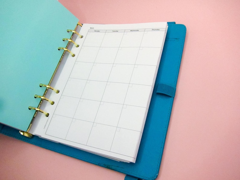 May include: A blue and turquoise planner with gold rings and a weekly calendar layout. The planner is open to a blank page with the days of the week labelled at the top.