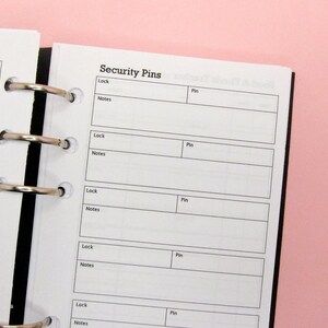 May include: A white page with a black binder and silver rings. The page has a title "Security Pins" and a table with columns for "Lock", "Notes", and "Pin".