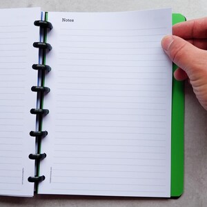 Puede incluir: Un cuaderno verde y negro con una encuadernaci&oacute;n de espiral negra. El cuaderno tiene p&aacute;ginas rayadas y la palabra "Notes" impresa en la portada.