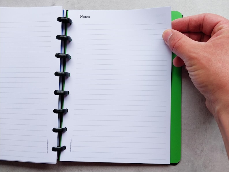 Puede incluir: Un cuaderno verde y negro con una encuadernaci&oacute;n de espiral negra. El cuaderno tiene p&aacute;ginas rayadas y la palabra "Notes" impresa en la portada.