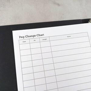 May include: A white "Peg Change Chart" page with a grid for recording data, held in a black binder. The chart includes columns for date, FR, length, and notes. The binder is open, revealing the chart and metal rings.