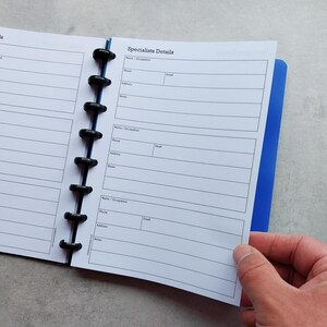 Puede incluir: Una agenda blanca con una cubierta azul y anillos negros. La agenda tiene una secci&oacute;n etiquetada como "Specialists Details" con campos para el nombre, la ocupaci&oacute;n, el tel&eacute;fono, el correo electr&oacute;nico, la direcci&oacute;n y las notas.