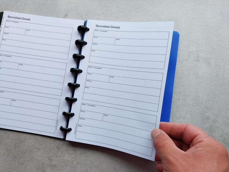 Puede incluir: Una agenda blanca con una cubierta azul y anillos negros. La agenda tiene una secci&oacute;n etiquetada como "Specialists Details" con campos para el nombre, la ocupaci&oacute;n, el tel&eacute;fono, el correo electr&oacute;nico, la direcci&oacute;n y las notas.