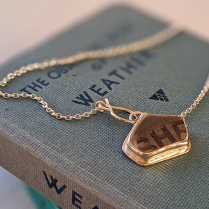 May include: A silver chain necklace with a pendant featuring a dark grey stone with the word "SHE" inscribed on it.