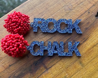 May include: A pair of earrings with red pom-poms and blue glitter words "ROCK CHALK"