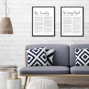 May include: Two black framed prints with white text on a white brick wall. The print on the left reads "The Family: A Proclamation to the World". The print on the right reads "The Living Christ: The Testimony of the Apostles". A gray couch with two blue and white patterned throw pillows is in the foreground.
