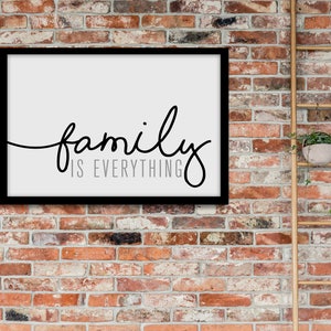 May include: A black framed print with the text "family is everything" in a cursive font. The print is hanging on a brick wall with a wooden ladder and potted plants to the right.