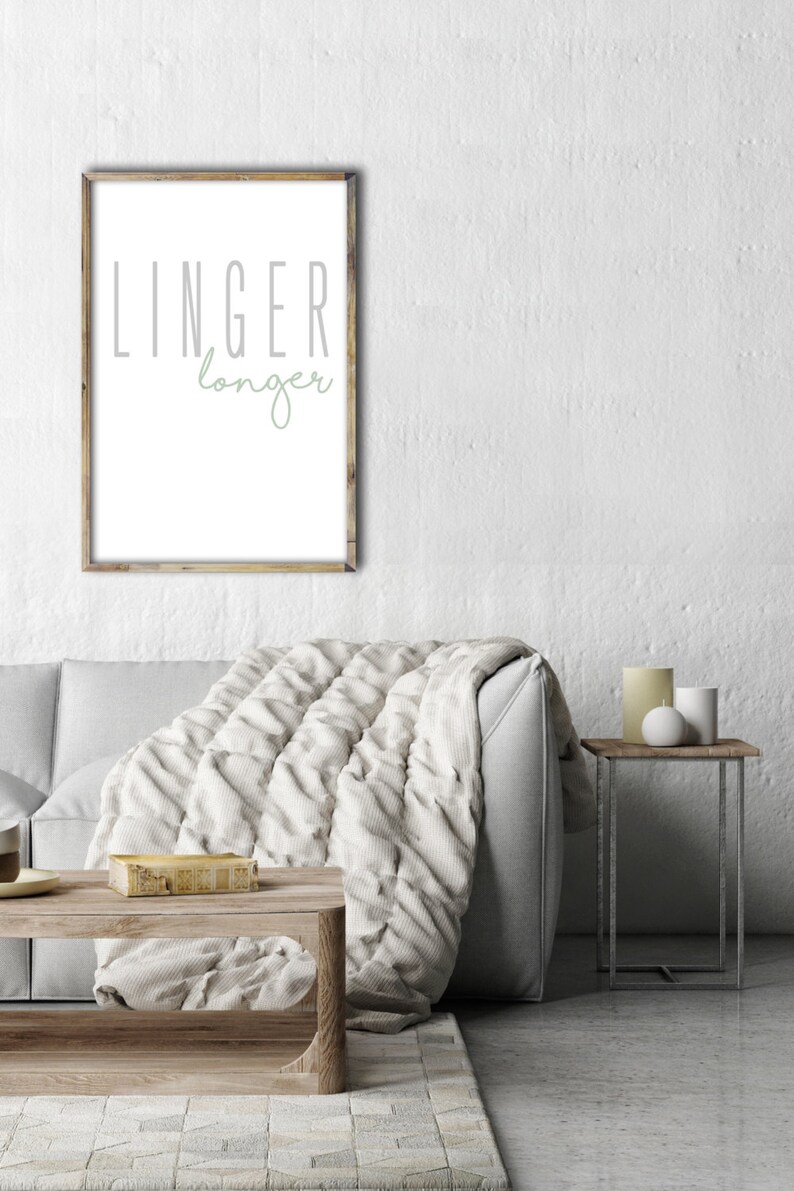 May include: A framed print with the text "LINGER longer" in a living room setting with a couch, throw blanket, and a side table with candles.