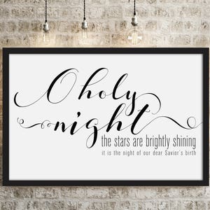 May include: A framed print with the words "O Holy Night" in elegant script. The text "the stars are brightly shining, it is the night of our dear Savior's birth" is also included. The print is displayed against a brick wall.