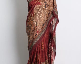 May include: A maroon silk saree with a gold and black paisley print. The saree is draped on a mannequin.