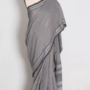 May include: A black and white chequered saree draped on a mannequin. The fabric features a fine gingham pattern throughout, complemented by a wide, intricate woven border with geometric motifs and a striped end piece in black and white.