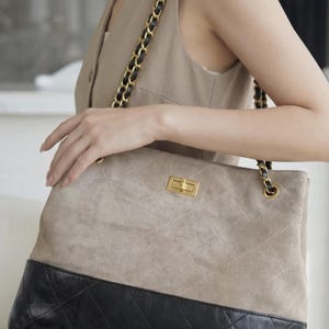 Pode incluir: Bolsa tote acolchoada bege e preta com uma al&ccedil;a de corrente dourada. A bolsa apresenta um padr&atilde;o de diamante no material bege semelhante a camur&ccedil;a e uma base de couro preta. Um fecho dourado prende a parte superior.