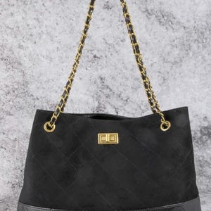 Pode incluir: Bolsa tote preta com al&ccedil;a de corrente dourada. A bolsa apresenta uma parte superior de camur&ccedil;a acolchoada e uma base de couro com costura de diamante. Um fecho retangular dourado est&aacute; centrado na frente.