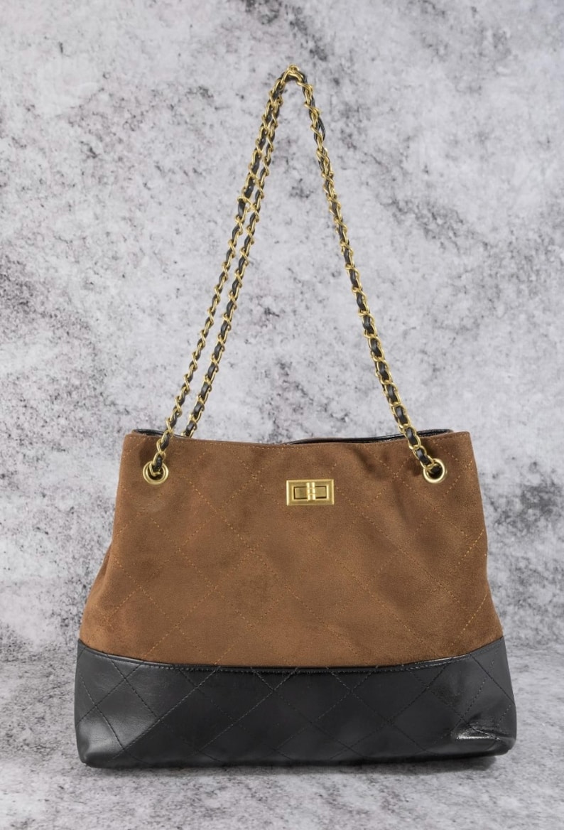 Pode incluir: Bolsa tote de camur&ccedil;a marrom com fundo de couro preto e al&ccedil;a de corrente dourada. A bolsa tem um padr&atilde;o acolchoado na camur&ccedil;a e um fecho dourado. Um acess&oacute;rio elegante.