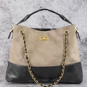 Pode incluir: Bolsa bege e preta com al&ccedil;a de corrente dourada. A bolsa tem uma parte superior de camur&ccedil;a bege acolchoada e uma parte inferior de couro preto. A al&ccedil;a &eacute; preta e a bolsa tem um fecho dourado.