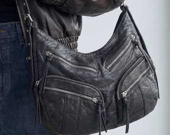 Bolsa hobo despojada com vários bolsos, em couro sintético, estilo motoqueiro anos 2000.