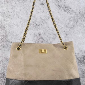 Pode incluir: Bolsa tote de camur&ccedil;a bege com base em couro preto. A bolsa apresenta um fecho dourado e al&ccedil;as de corrente com detalhes em preto. A se&ccedil;&atilde;o de camur&ccedil;a bege tem um padr&atilde;o acolchoado.