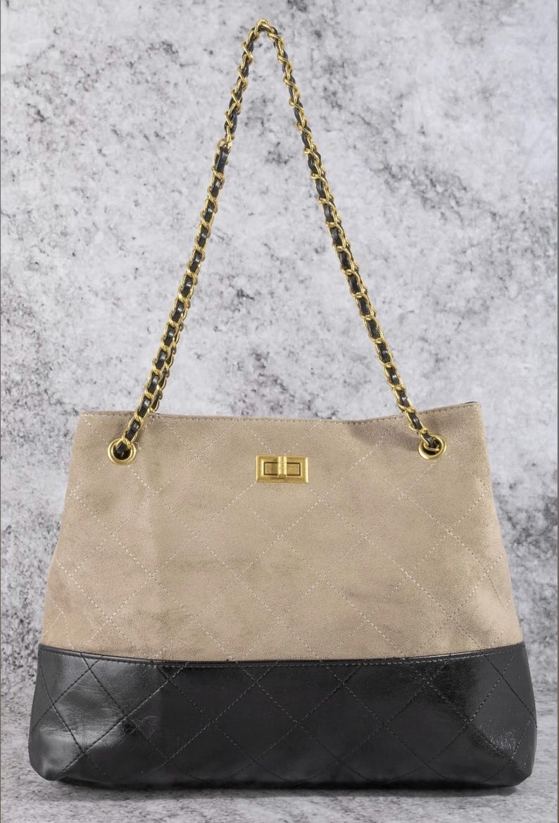 Pode incluir: Bolsa tote de camur&ccedil;a bege com base em couro preto. A bolsa apresenta um fecho dourado e al&ccedil;as de corrente com detalhes em preto. A se&ccedil;&atilde;o de camur&ccedil;a bege tem um padr&atilde;o acolchoado.