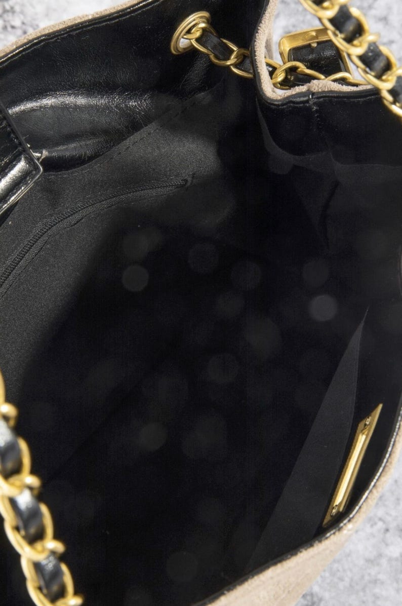 Pode incluir: Uma vista de perto do interior de uma mala bege com um interior preto. A mala apresenta uma al&ccedil;a de corrente dourada e detalhes dourados. H&aacute; um bolso interior com z&iacute;per.