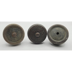 May include: Three antique, weathered metal wheels. The wheels are circular with a central hub. One wheel has an ornate, engraved design. The wheels are various shades of brown and gray, suggesting age and use. They are set against a plain white background.