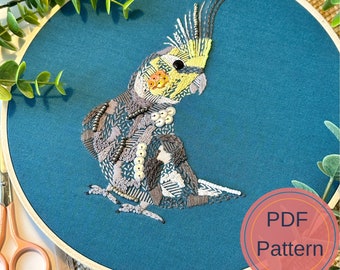 May include: Hand-stitched embroidery art featuring a detailed cockatiel with a person. The bird has yellow, gray, and white feathers, and the person is in shades of gray and white. The artwork is set against a teal background within a wooden hoop. The text "PDF Pattern" is in a circle.