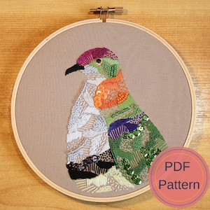 May include: Embroidered bird design on a beige fabric background. The bird is made of colorful beads and sequins. The design is framed in a wooden hoop. The text "PDF Pattern" is on a pink circle.
