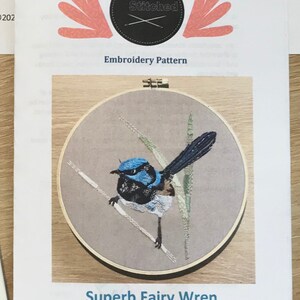 May include: Embroidery pattern for a Superb Fairy Wren, a small blue bird with a black head and white belly, perched on a branch with green leaves. The pattern is from Curiously Stitched and is copyrighted 2020.
