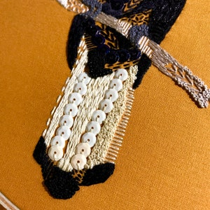 May include: Close-up of a black and white embroidered design with white sequins on a mustard yellow fabric.
