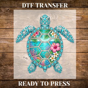 May include: A DTF transfer featuring a sea turtle design. The turtle has a turquoise shell adorned with gemstones. The center of the shell showcases a tropical scene with pink hibiscus flowers, coral, and ocean elements. The text "DTF TRANSFER" and "READY TO PRESS" are at the top and bottom.