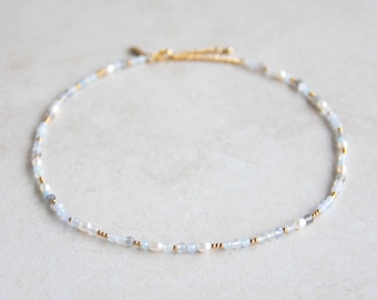Könnte beinhalten: Eine zarte goldene Kettenkette mit kleinen blauen und weißen Perlen. Die Kette besteht aus verschiedenen Materialien, darunter Gold, Glas und Perlen.