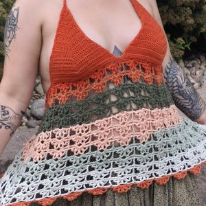 May include: A handmade crochet halter top in shades of orange, green, peach, and white. The top features a halter neck and a flared, openwork design. The bottom edge has a scalloped trim.