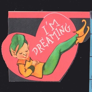 May include: Vintage Valentine's Day card featuring a cartoon elf figure. The elf, with green hair and green pants, is reclining on a red heart. The heart has the words "I'M DREAMING" in white. The elf wears an orange shirt and yellow shoes.