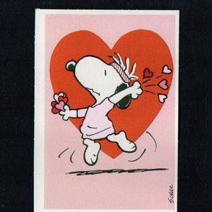 May include: A Snoopy Valentine's Day card featuring Snoopy in a pink shirt, headband, and white shoes, holding a heart-shaped flower and blowing heart-shaped kisses. A large red heart is in the background. The artist's signature, Schulz, is in the lower right corner.