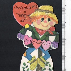 May include: A vintage Valentine's Day card featuring a cartoon scarecrow holding hearts that say "Don't give me a hang-up" and "Be my Valentine".