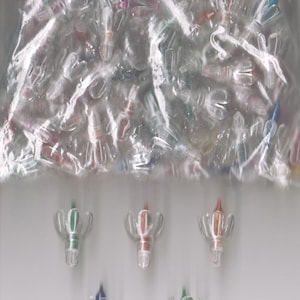 May include: A clear plastic bag filled with small, clear plastic Christmas light bulbs. Six bulbs are arranged below the bag, with green, red, and blue accents. The bulbs have a unique, stylized shape.