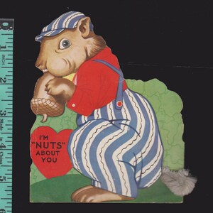 May include: Vintage Valentine's Day card featuring a cartoon squirrel wearing a striped cap and overalls, holding an acorn. The squirrel is set against a green backdrop, with a red heart that reads "I'M 'NUTS' ABOUT YOU".